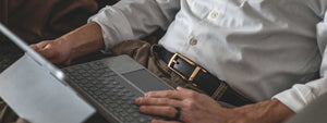 male wear Tonywell ratchet dress belt sitting with hands on computer wearing white class shirt khaki pants